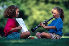 Two girls, one holding the music for the other who plays the clarinet